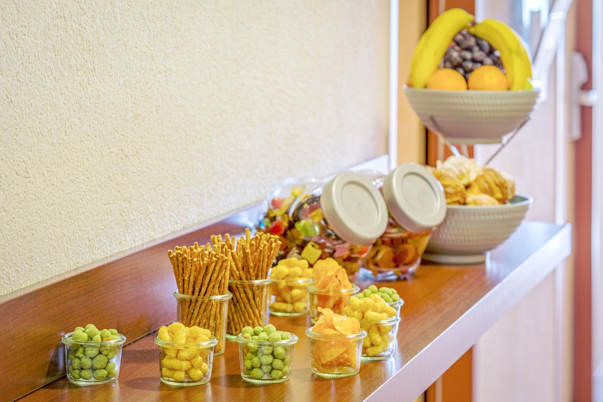 Ein Buffet mit verschiedenen Speisen, darunter Brezeln, grüne und gelbe Snacks sowie eine Obstschale.