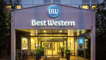 Ein Hotel Eingang mit einem Schild mit der Aufschrift 'Best Western', einer Glastür und Zimmerpflanzen.