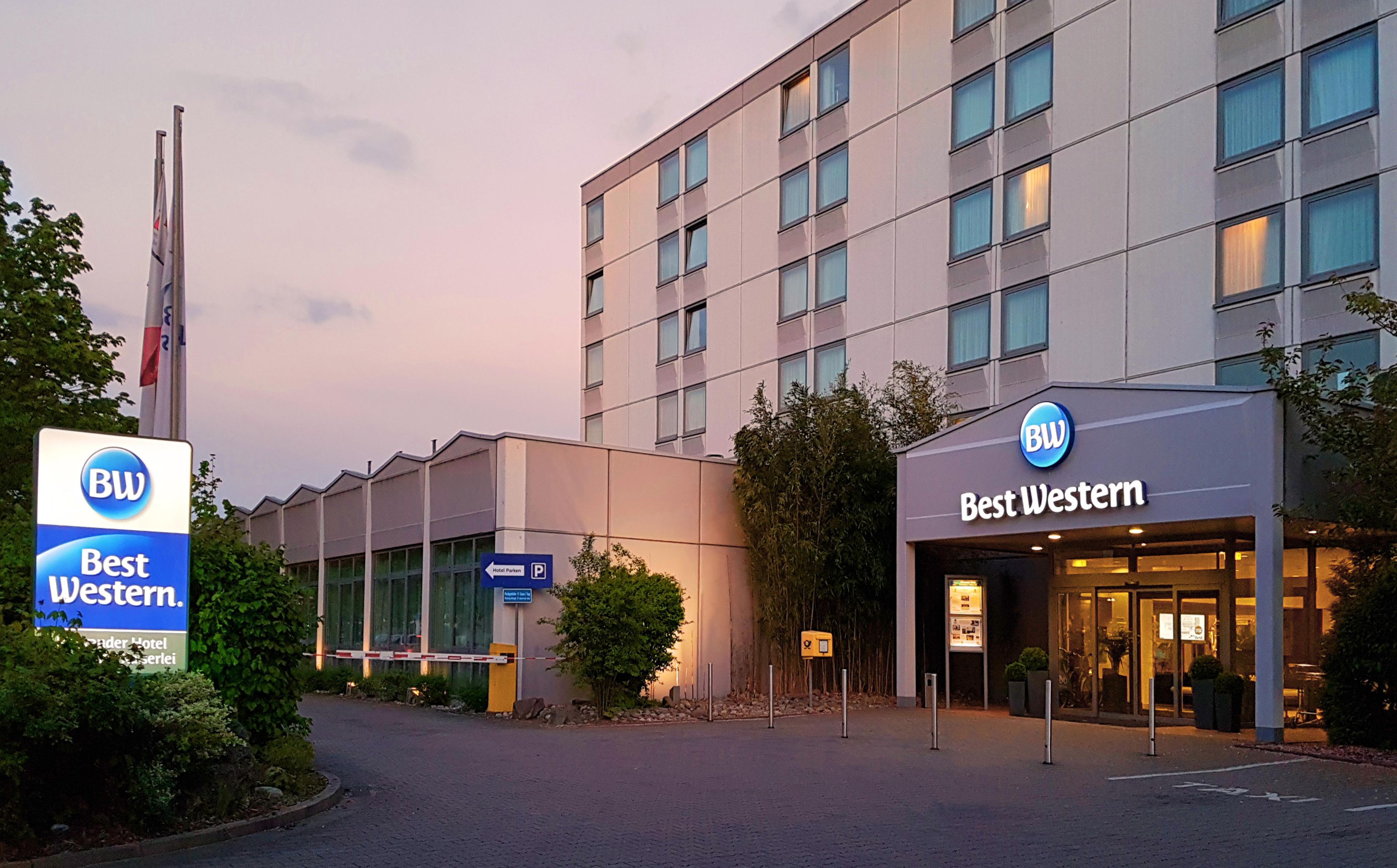 L’entrée d’un hôtel, avec une enseigne indiquant « Best Western », un panneau de signalisation pour le stationnement et un mât de drapeau.