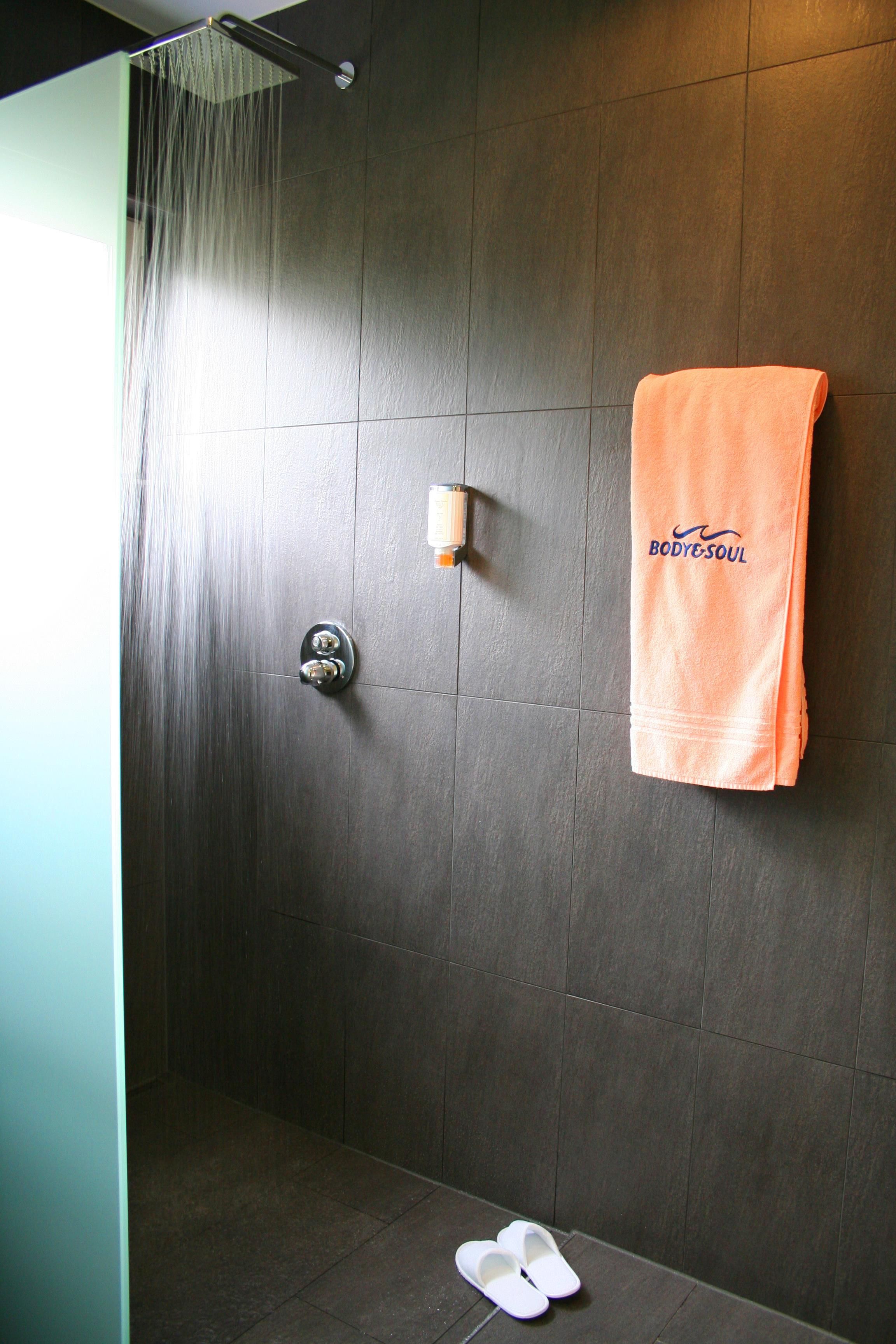 Eine Dusche mit Glastür, ein Handtuchhalter mit Handtuch und ein Seifenspender an der Wand.