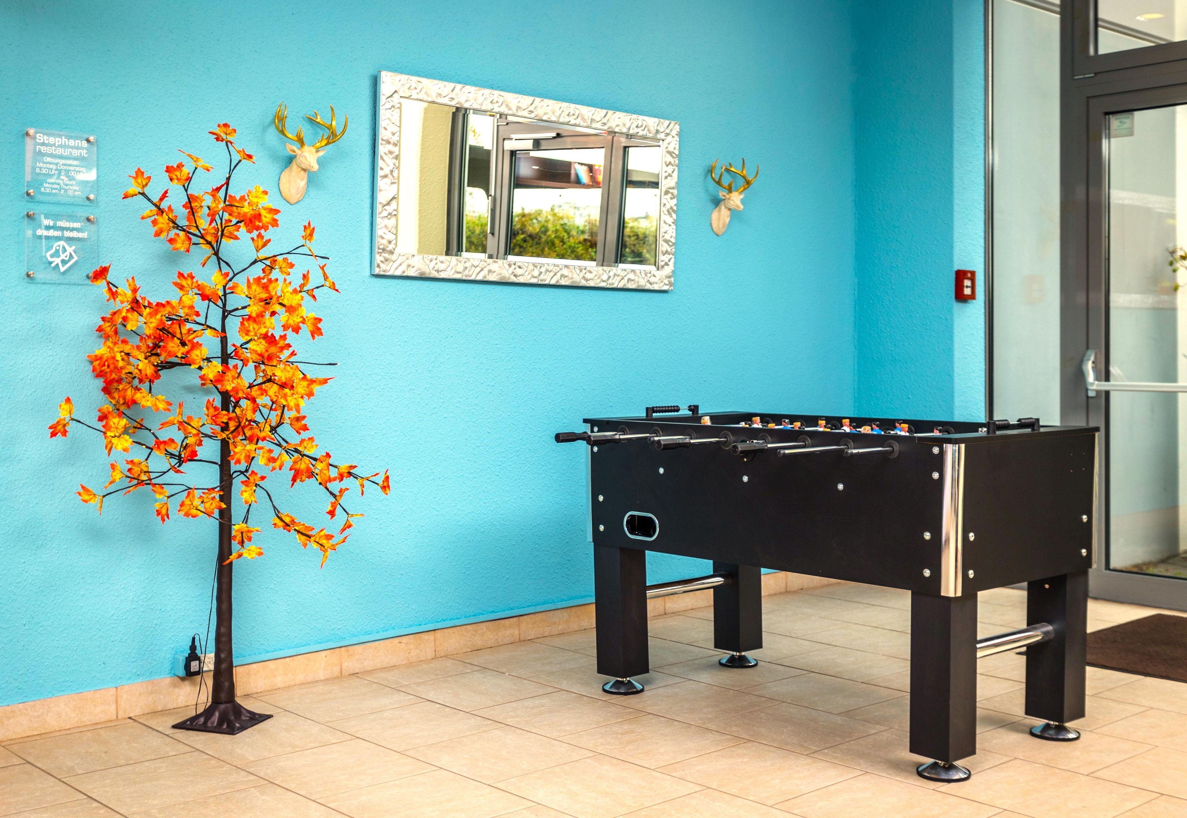 A room with a foosball table, a wall-mounted mirror, and autumn leaves decoration.