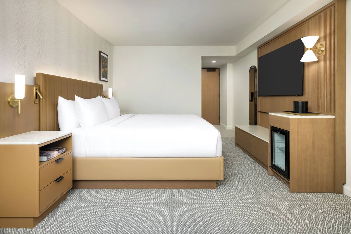 Ein Hotelzimmer mit Bett, Nachttischen, Fernseher und einer Minibar.