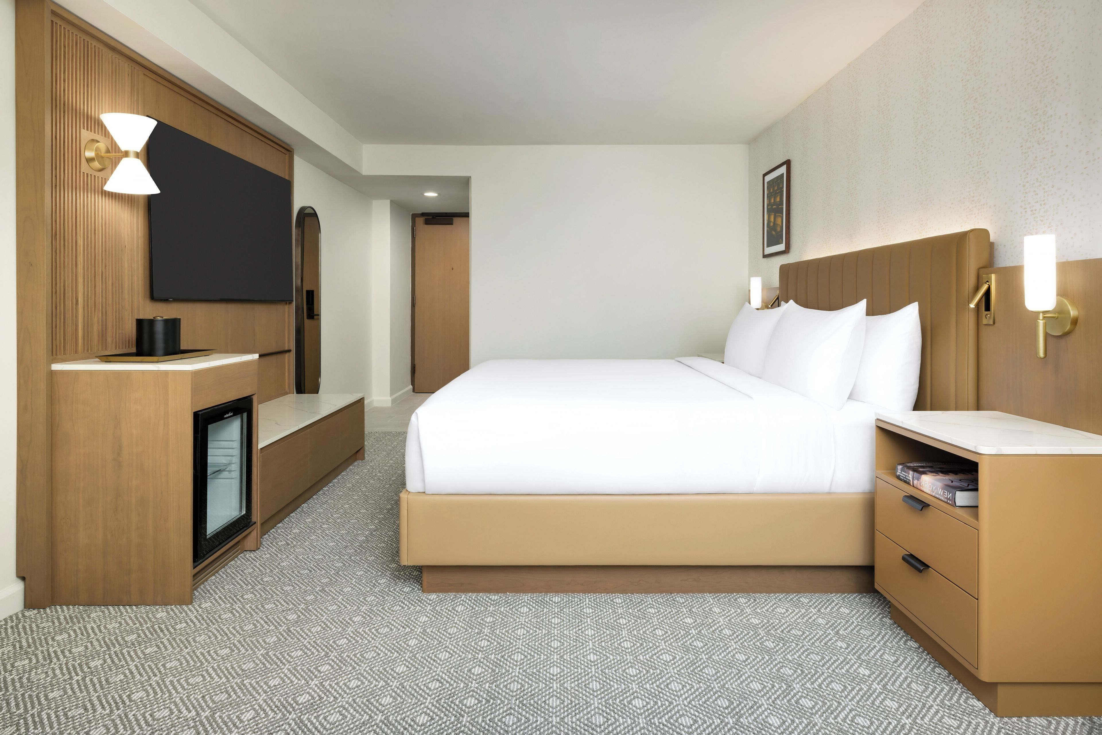Een hotelkamer met een bed, een televisie, een bureau en een minibar.