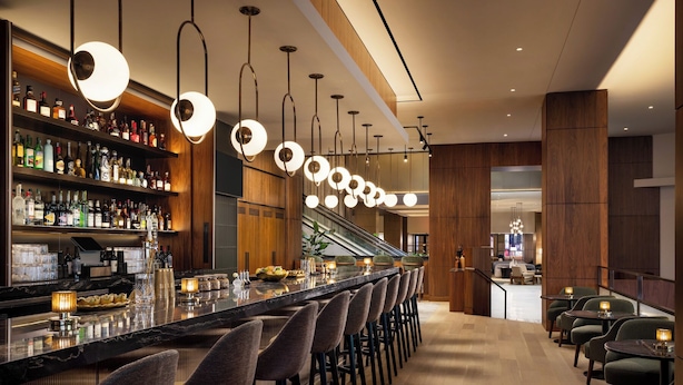 Eine moderne Bar mit einer langen Theke, mehreren hängenden Leuchten und einer Auswahl an Flaschen in Regalen.