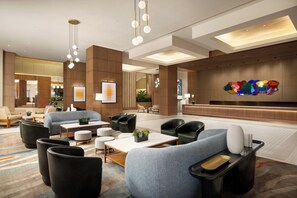 Un vestíbul d'hotel modern amb zones d'estar, una taquilla d'emissió i obres d'art a les parets.