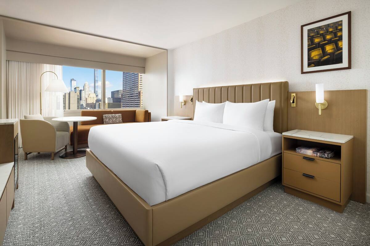 Ein Hotelzimmer mit einem großen Bett, einem Schreibtisch, einem Stuhl und Blick auf die Skyline der Stadt.