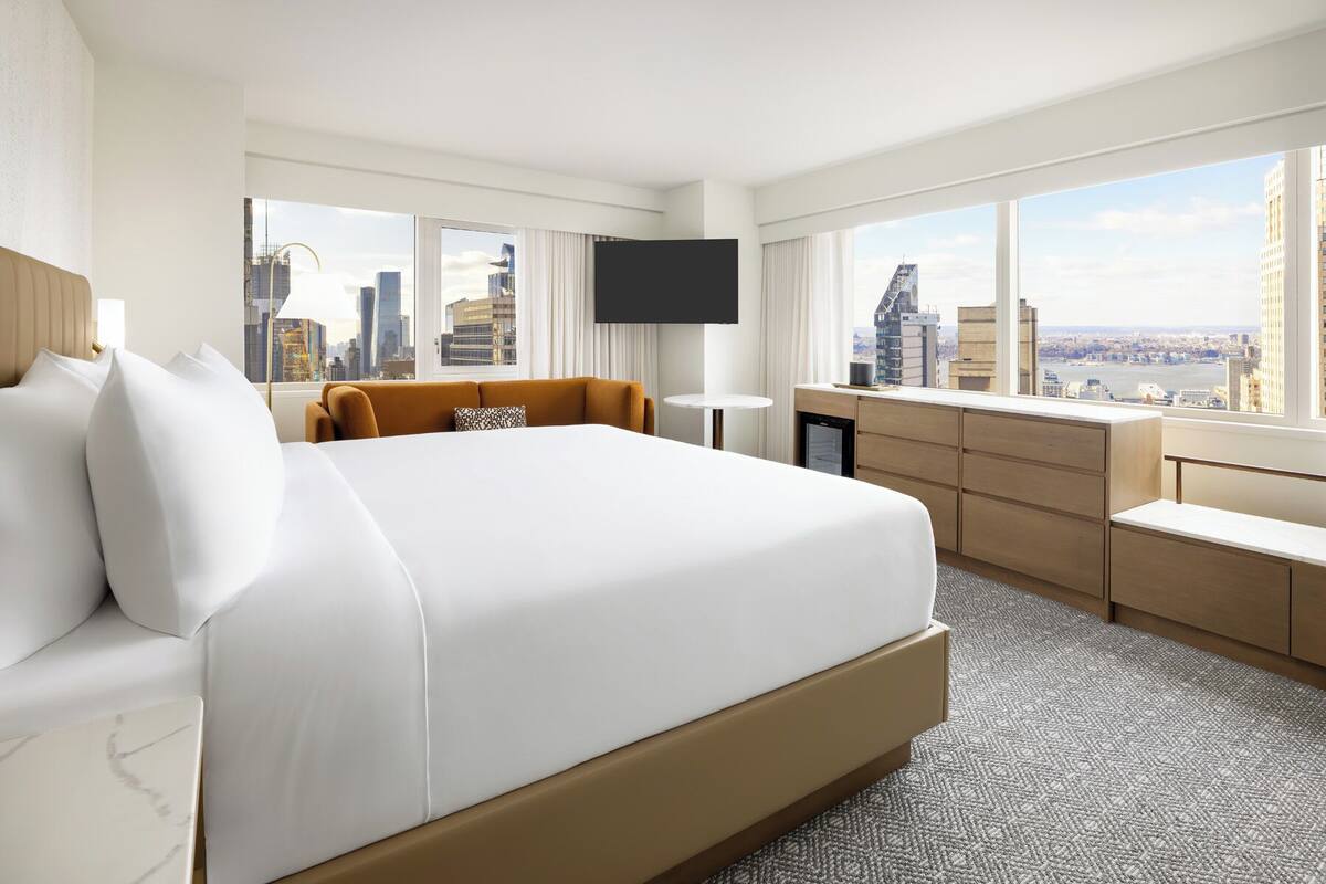Ein Hotelzimmer mit einem großen Bett, einem Schreibtisch, einem Fernseher und Blick auf die Stadt.