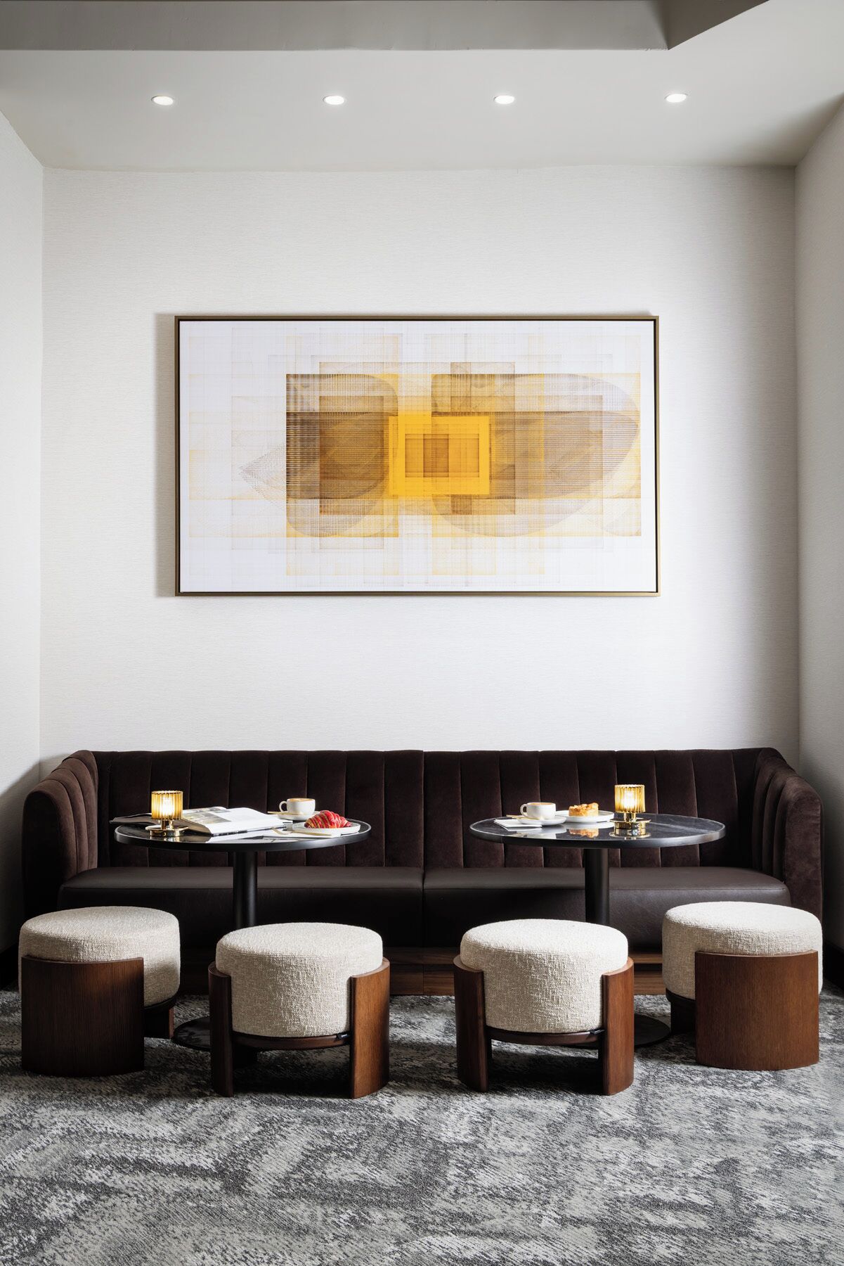 A modern living room with a dark brown sofa, three matching ottomans, a coffee table, and a framed abstract artwork on the wall.