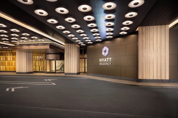 En modern entré till ett Hyatt Regency-hotell, med en tydlig logotyp, en glashiss och ett väl upplyst tak med runda lampor.