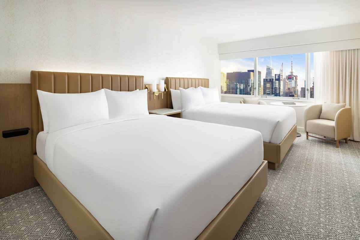 Ein Hotelzimmer mit zwei Betten, Blick auf eine Stadtlandschaft und einer kleinen Sitzecke.