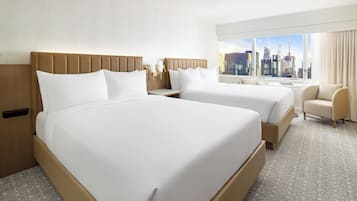 Una habitación de hotel con dos camas, vista al horizonte urbano y una pequeña zona de estar.