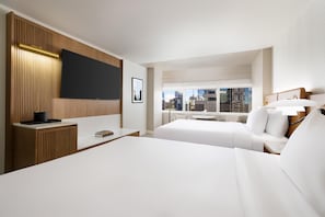 Ett hotellrum med två sängar, en platt-TV, ett skrivbord med en lampa och utsikt över staden.