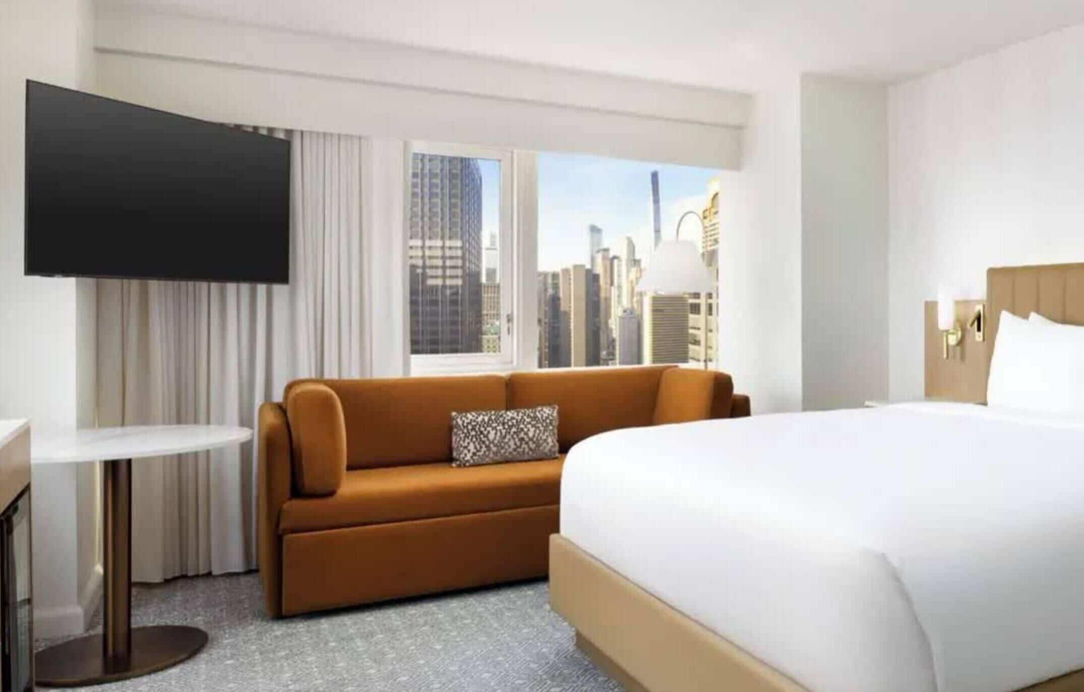 A hotel room with a bed, a sofa, a TV, and a city view.