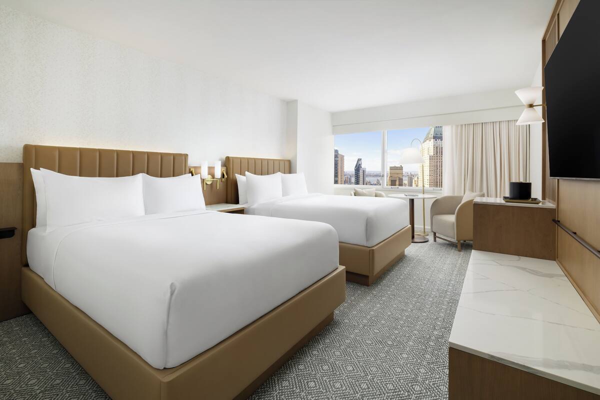 Ein Hotelzimmer mit zwei Betten, einem Schreibtisch und Blick auf die Stadt.