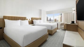 A hotel room with two beds, a desk, and a view of the city.