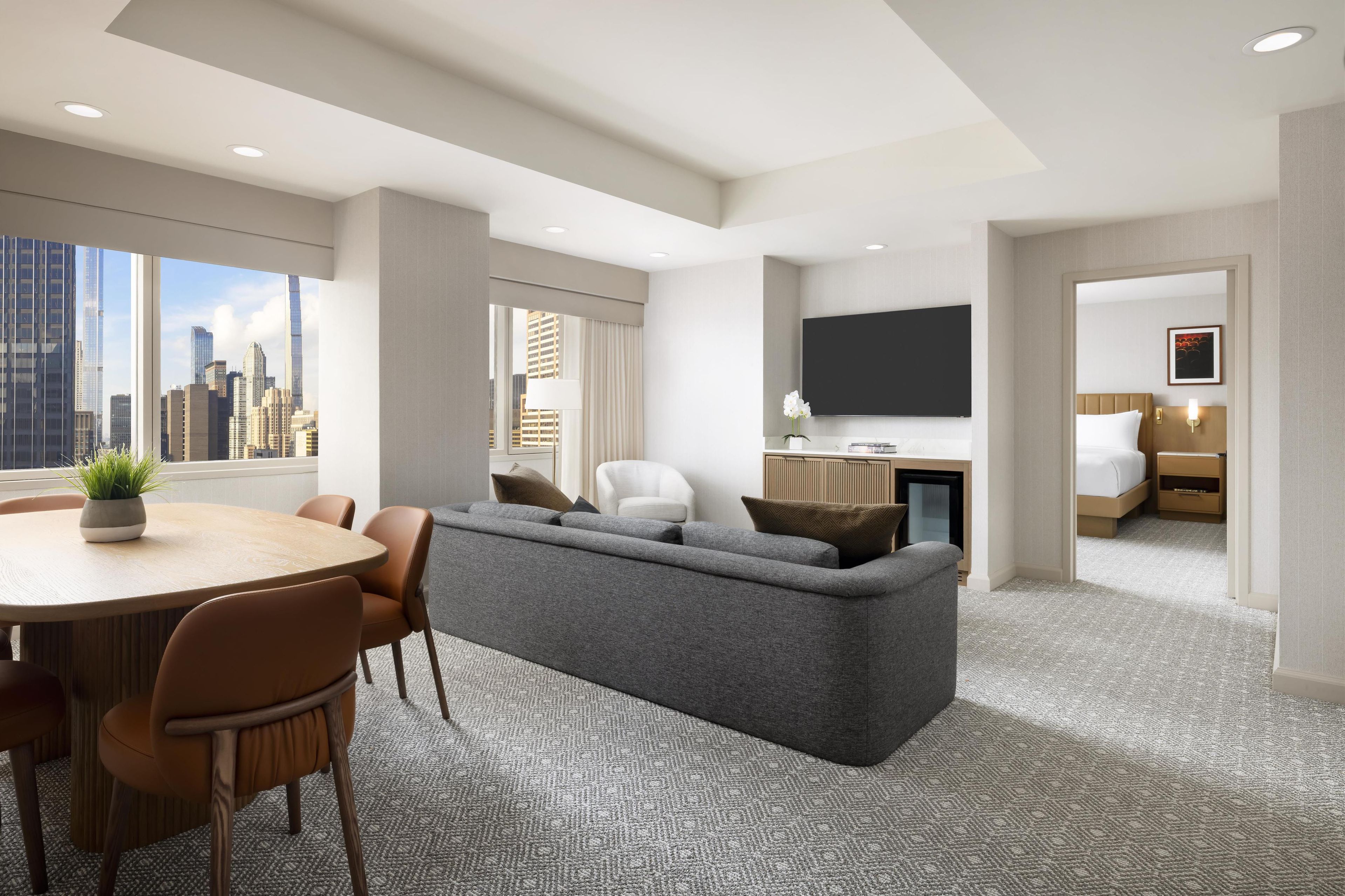 Une chambre d’hôtel moderne avec vue sur la ville, comprenant un canapé, une table à manger avec des chaises, une télévision et un lit.