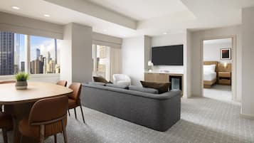 Une chambre d’hôtel moderne avec vue sur la ville, comprenant un canapé, une table à manger avec des chaises, une télévision et un lit.