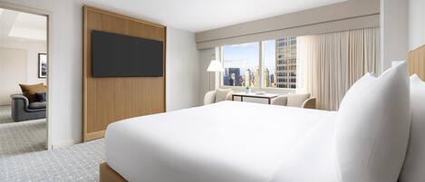 Habitación de hotel con una cama grande, un escritorio, una silla, un televisor montado en la pared y vistas de la ciudad a través del ventanal.