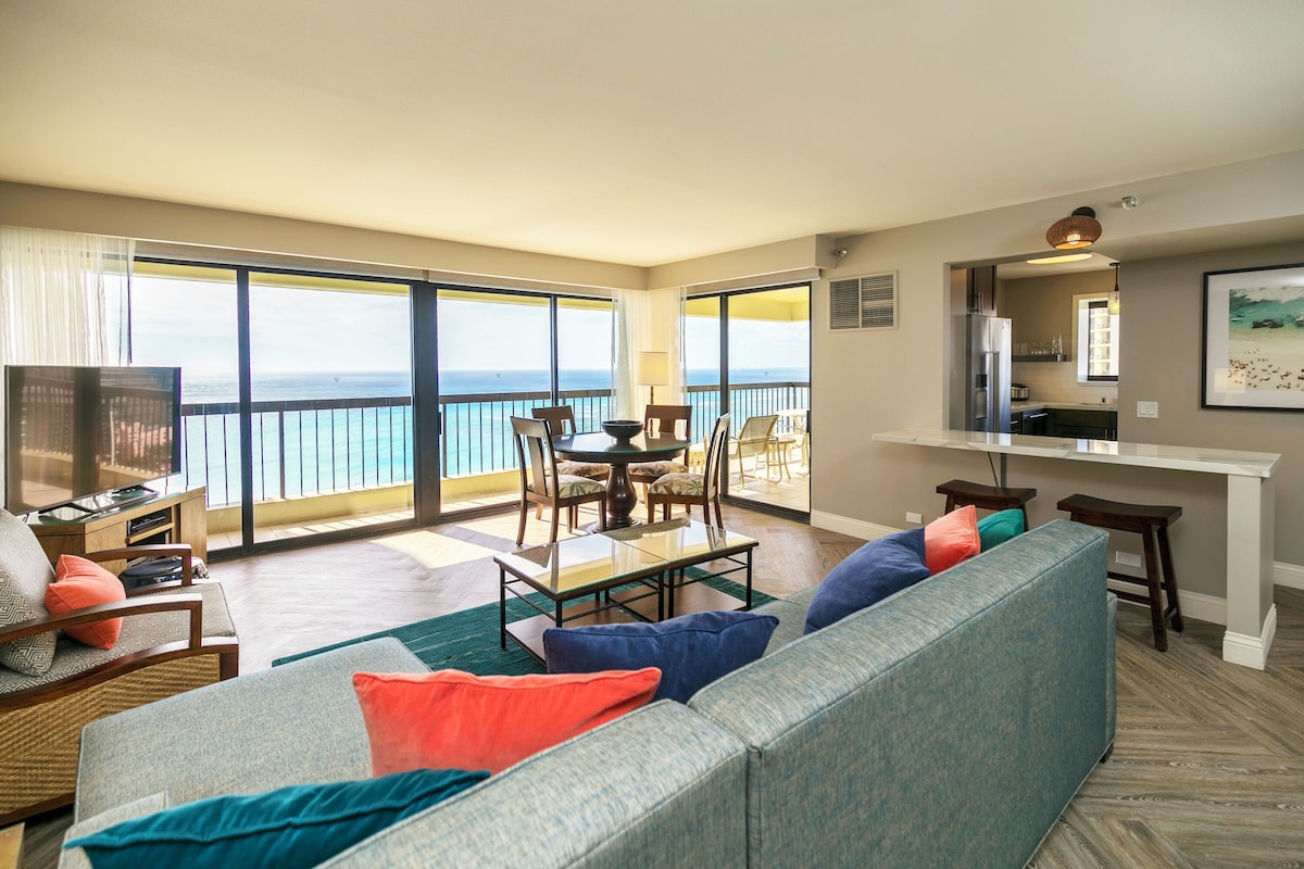 A spacious living area with a balcony, a dining table, and a kitchen area.