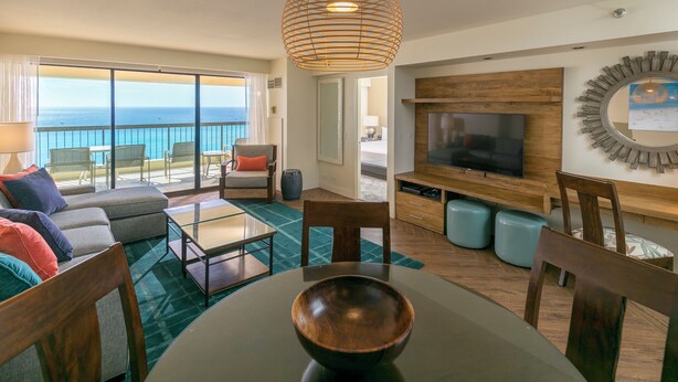 A modern living room with a large TV, comfortable seating, and a view of the ocean. - Aston Waikiki Beach Tower (Honolulu)
