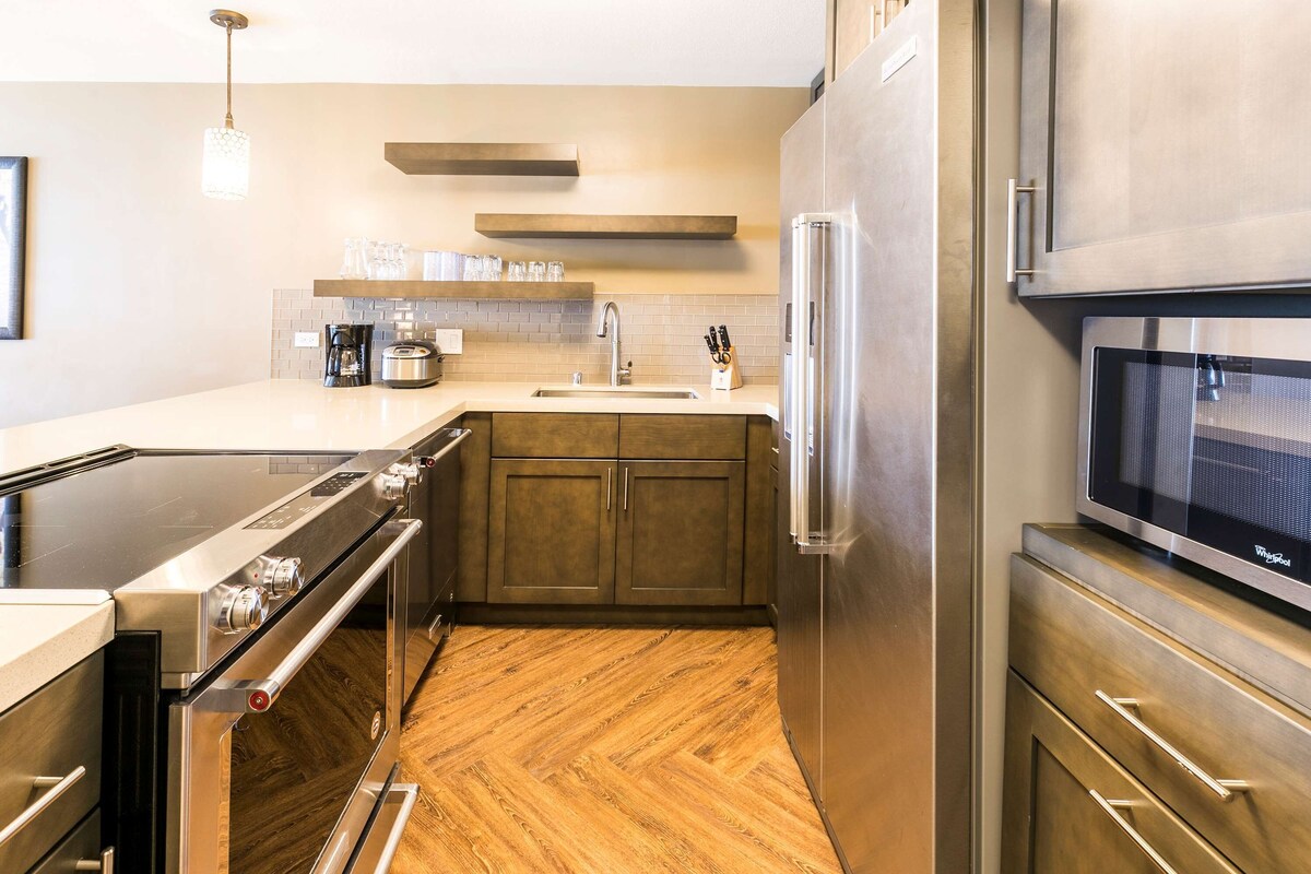 Cocina moderna con refrigerador de acero inoxidable, microondas y horno. Cuenta con gabinetes de madera y piso con estampado en espiga.
