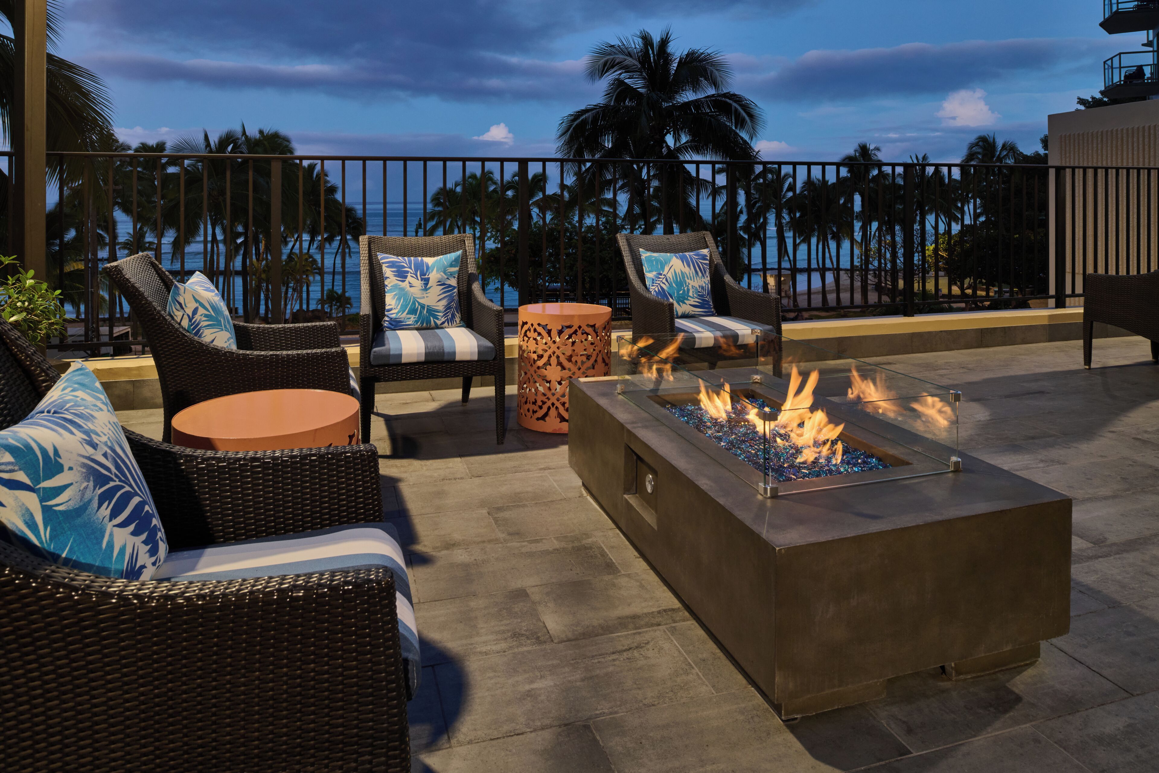 A rooftop terrace with wicker furniture, a fire pit, and a view of the ocean.