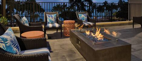 A rooftop terrace with wicker furniture, a fire pit, and a view of the ocean.
