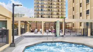 A rooftop pool area with lounge chairs and a surfboard, surrounded by high-rise buildings. - Aston Waikiki Beach Tower (Honolulu)