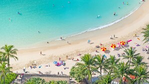 A beach with clear turquoise water, palm trees, and people sunbathing and swimming. - Aston Waikiki Beach Tower (Honolulu)