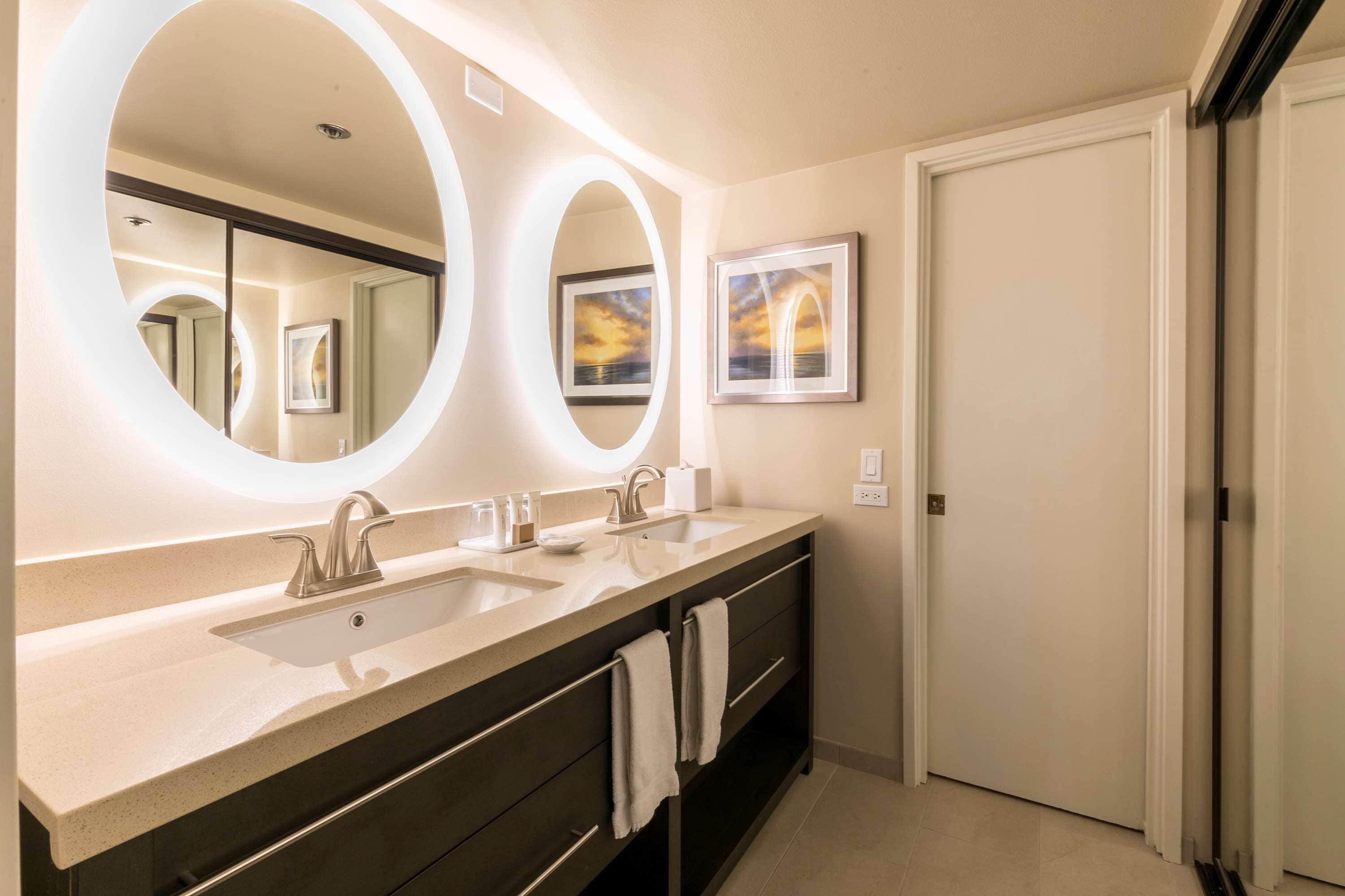 Un baño moderno con dos lavamanos, espejos grandes y un cuadro en la pared.