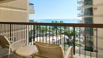 A balcony with wicker furniture, a view of the ocean, and a building with multiple balconies.