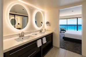 A modern bathroom with two sinks, large mirrors, and a view of a balcony with a bed. - Aston Waikiki Beach Tower (Honolulu)