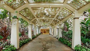 A covered walkway with a stone floor, flanked by lush greenery and white flowers. - Aston Waikiki Beach Tower (Honolulu)