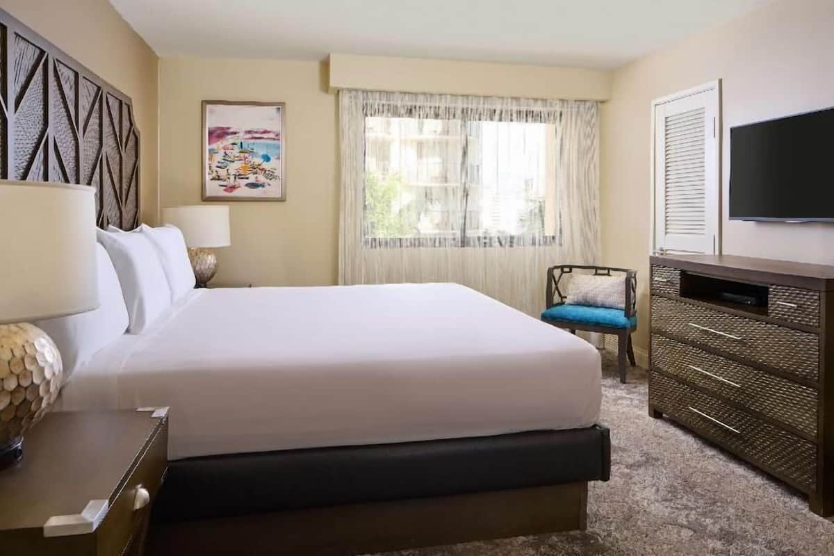 Een hotelkamer met een groot bed, een televisie, een kaptafel, een stoel en een raam met gordijnen.