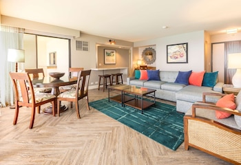 A modern kitchen with a stainless steel refrigerator, microwave, and oven. There are wooden cabinets and a herringbone-patterned floor. at Aston Waikiki Beach Tower