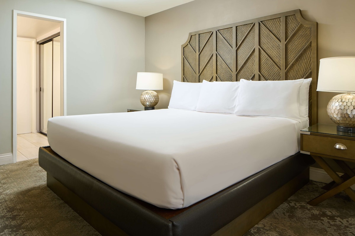A neatly made bed with a headboard, a bedside table with a lamp, and a carpeted floor.