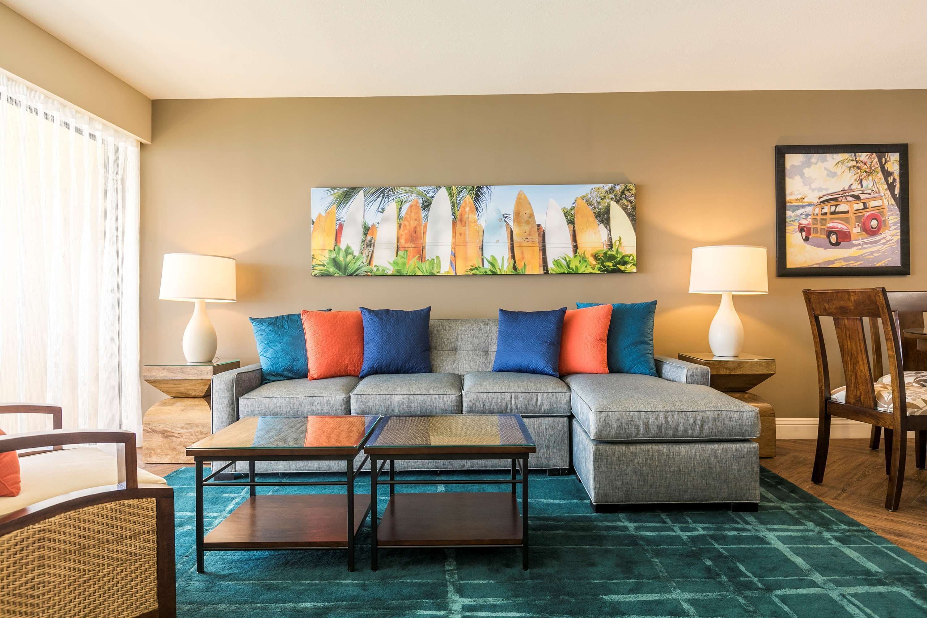 A living room with a sectional sofa, two side tables with lamps, a coffee table, and a painting of surfboards on the wall.