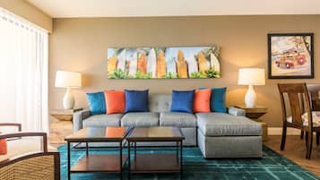 A living room with a sectional sofa, two side tables with lamps, a coffee table, and a painting of surfboards on the wall.