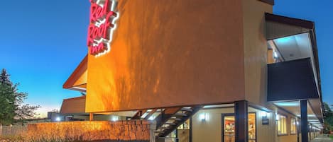 A Red Roof Inn with a modern architectural design, featuring a prominent neon sign, a lobby area, and a staircase leading to the entrance.
