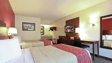 Una habitación de hotel con dos camas, un escritorio, un televisor y un espejo.