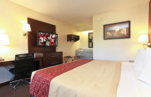 A hotel room with a bed, desk, chair, TV, and a bathroom area.
