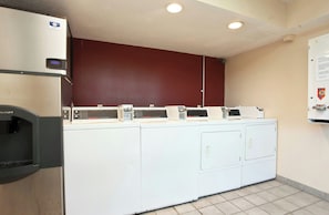 A laundry facility with multiple washing machines and dryers, a refrigerator, and a wall-mounted sign.