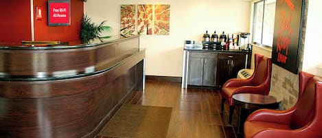 A reception area with a curved wooden desk, a coffee station, and red leather seating.