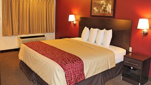 A hotel room with a large bed, two bedside lamps, a heater, a window with curtains, and a framed picture on the wall.