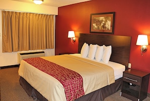 Habitación de hotel con una cama grande, dos lámparas de noche, un calefactor, una ventana con cortinas y un cuadro en la pared.