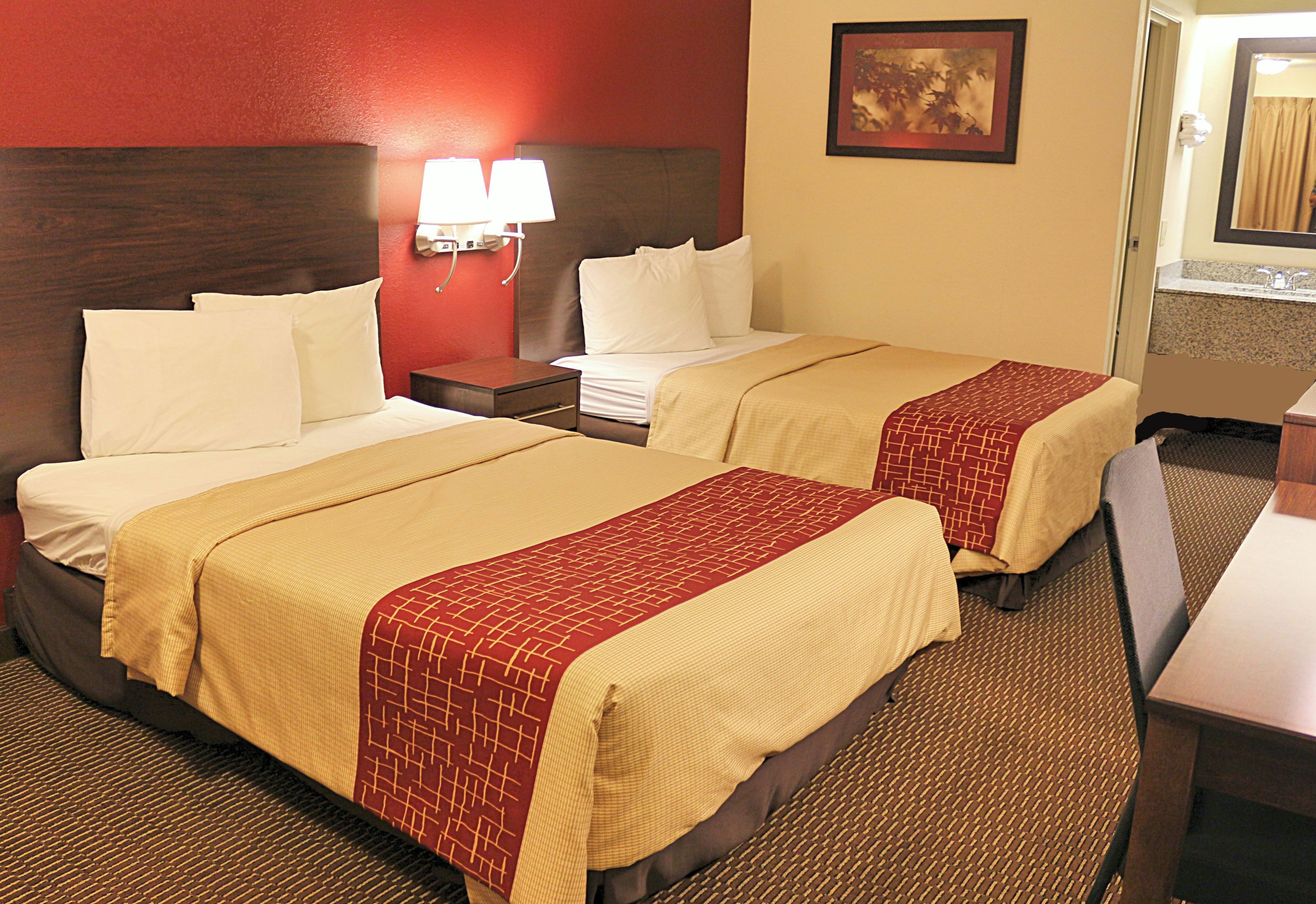 A hotel room with two beds, a nightstand, a lamp, and a bathroom visible through an open door.