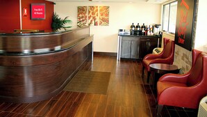 A reception area with a curved wooden counter, a coffee station, and red leather seating.