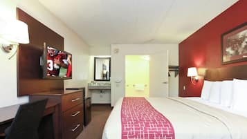 Una habitación de hotel con cama, escritorio, televisor, espejo y baño.