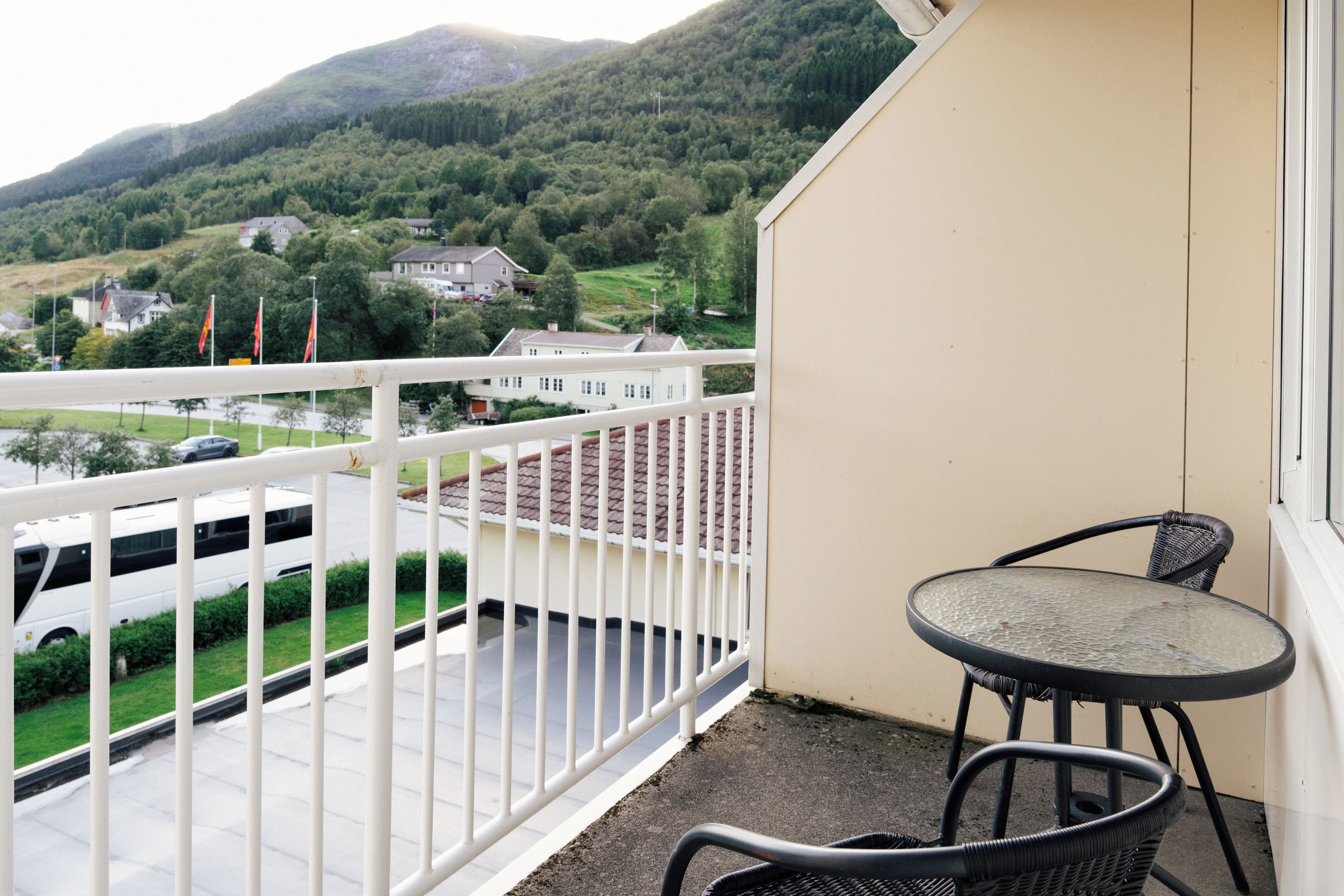 A balcony with a view of a mountain, a white fence, and a table with chairs.