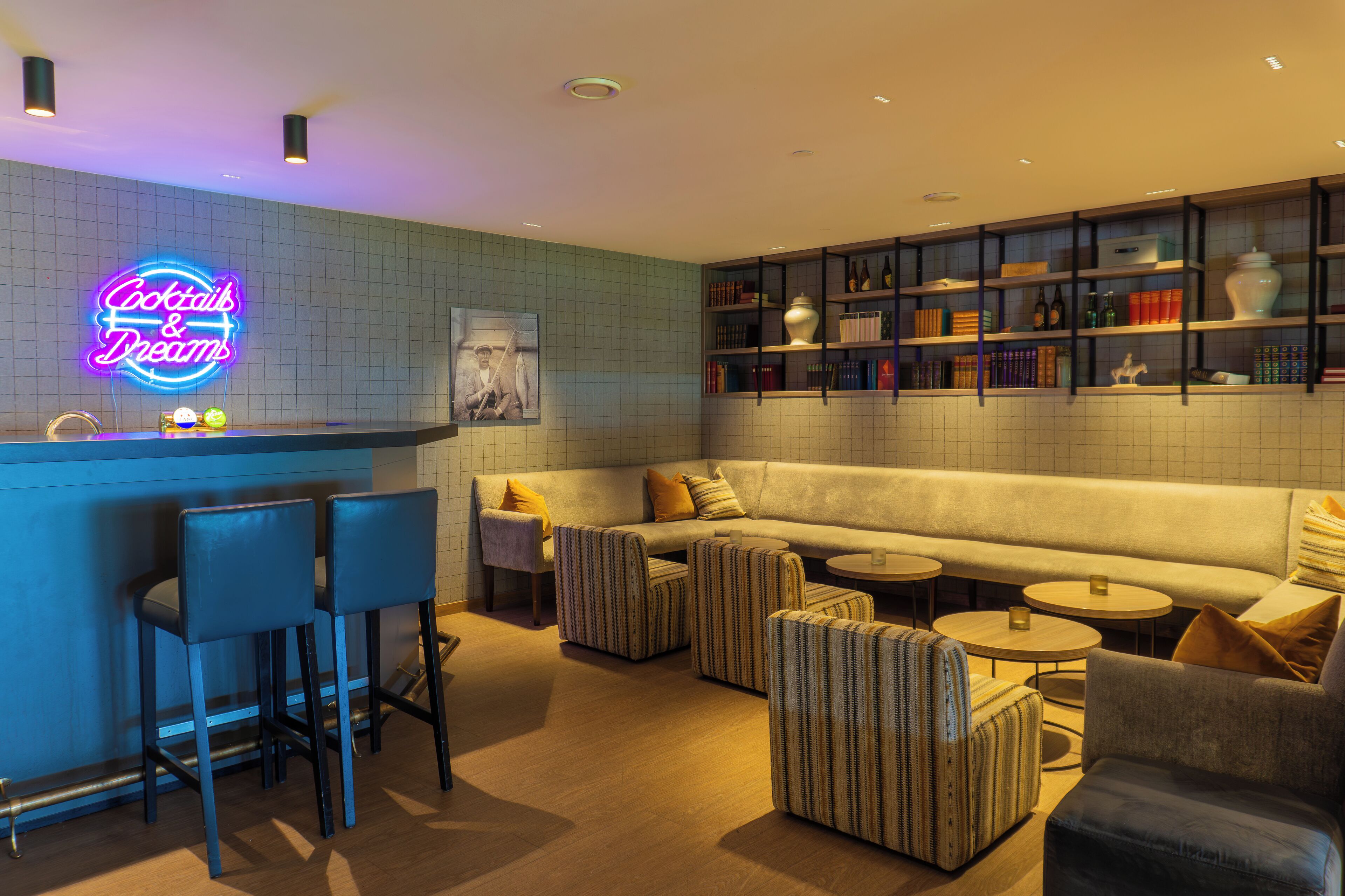 A modern lounge area with a neon sign, a bar, seating, and a bookshelf.